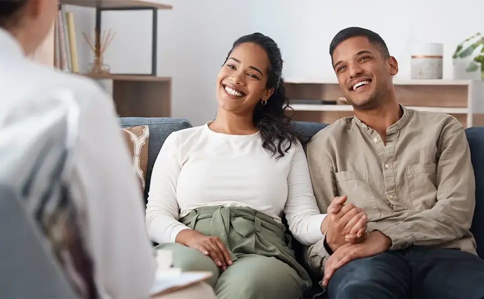 Young mixed couple smiling and holding hands at a consultation.