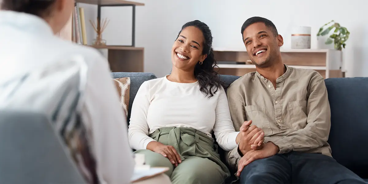 Young mixed couple smiling and holding hands at a consultation.