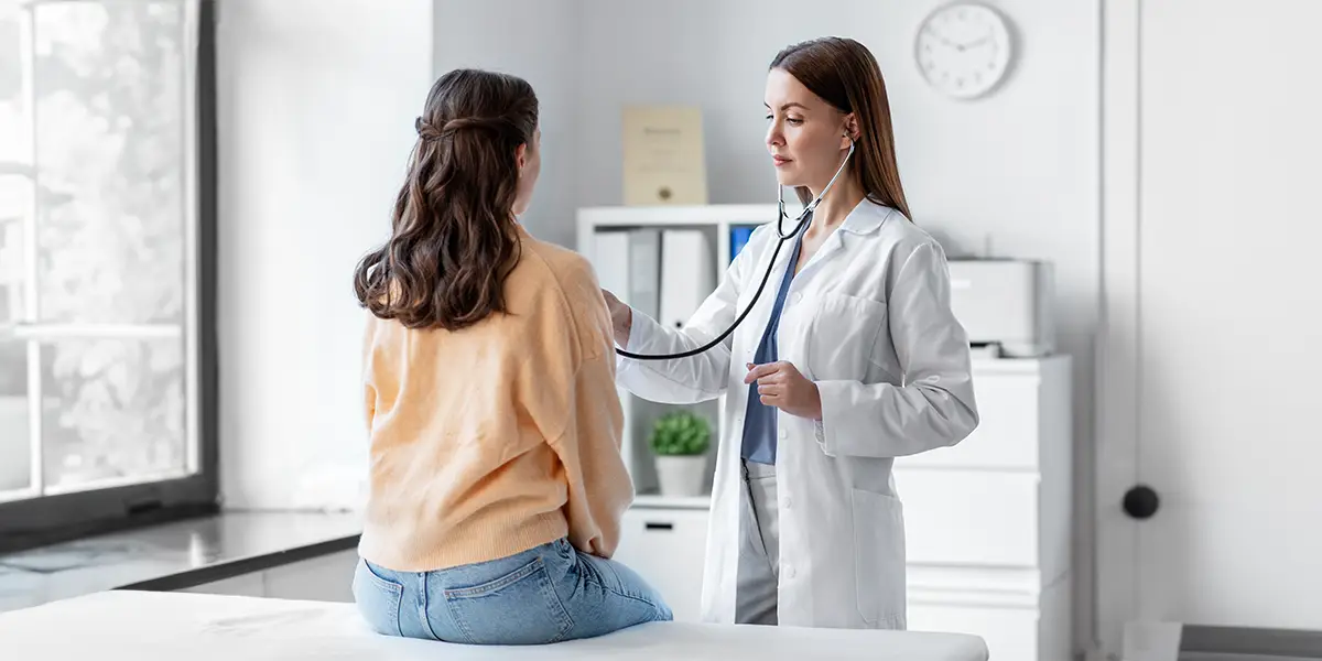 Young caucasian female doctor using a stethoscope to check her young female patient.
