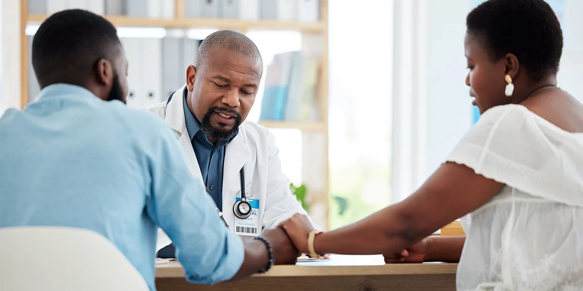 Black couple holding hands talking to a male doctor