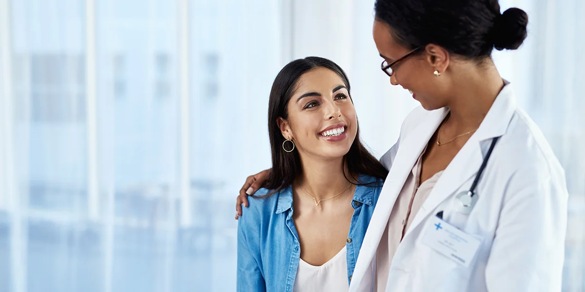 Ethnically ambiguous young woman smiling and being comforted by her female doctor