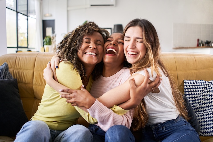 Three young women hugging on a sofa