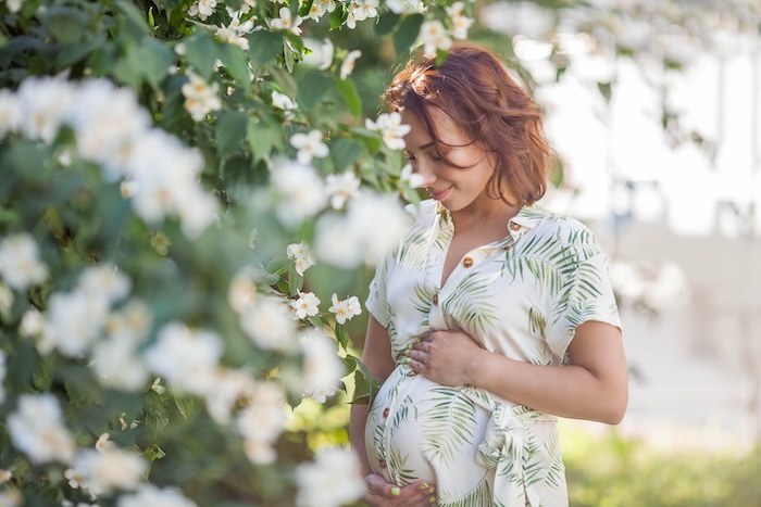 Pregnant woman next to a big bush of white flowers outside