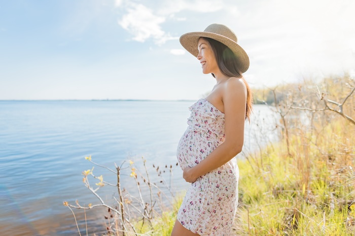 Pregnant Asian woman outside looking out on a lake 