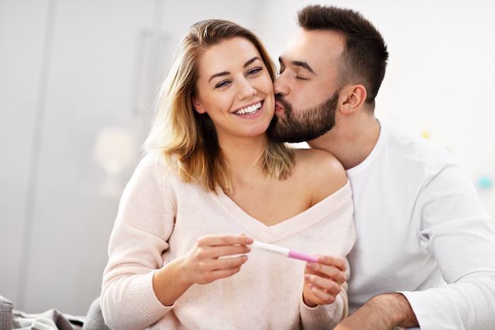 Young caucasian couple smiling and holding a positive pregnancy test