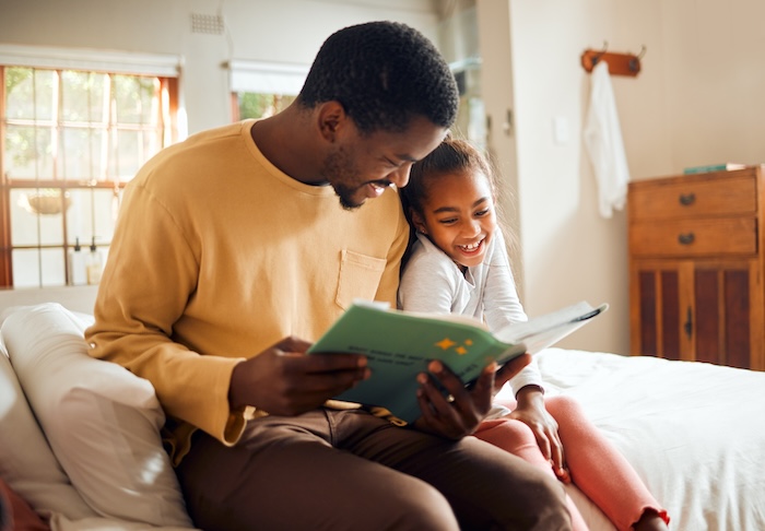 Younger black father reading a book to his daughter. 