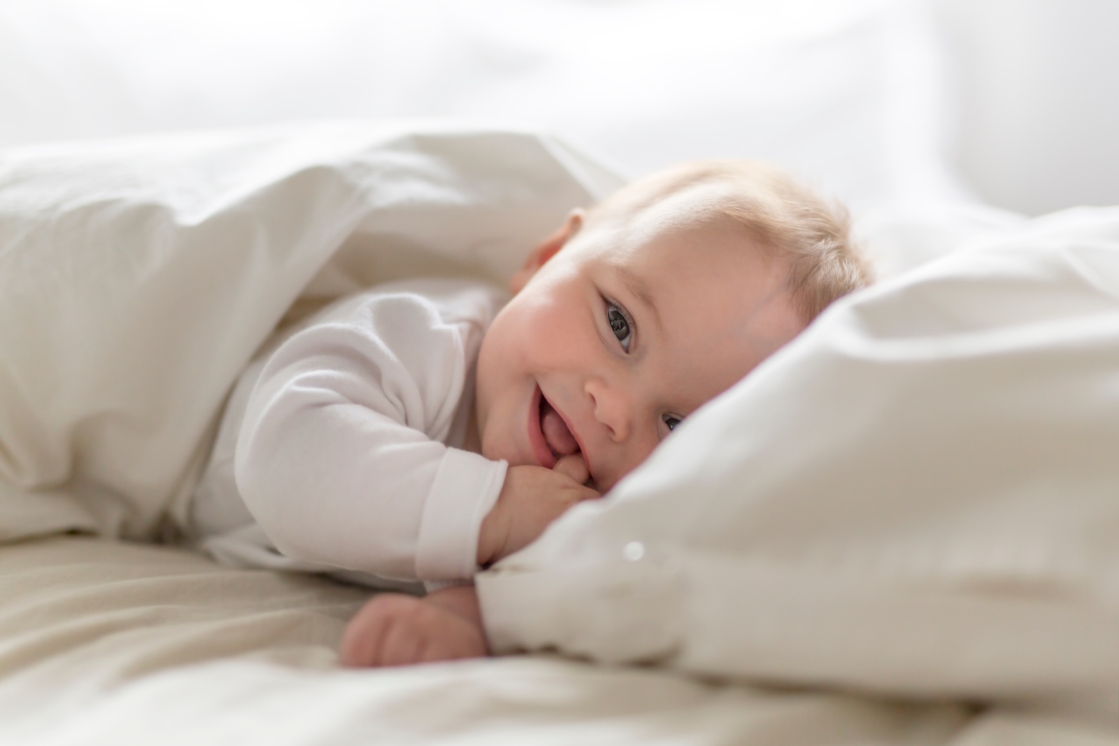 Young smiling baby laying in a white bed.
