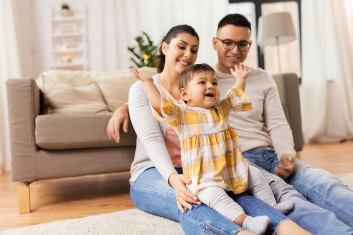 Happy, multiracial toddler raising their hands while sitting on their mother. 
