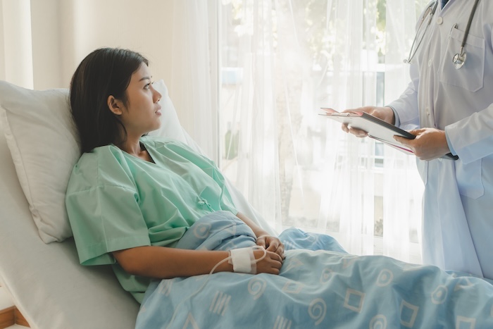 young woman sitting on the bed and looking outside window in hospital worry about her egg donation.