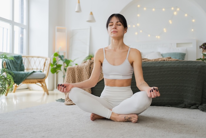 Yoga mindfulness meditation. Young healthy woman practicing yoga in living room at home. Woman sitting in lotus pose meditating smiling relaxing indoor. Girl doing breathing practice. Yoga at home